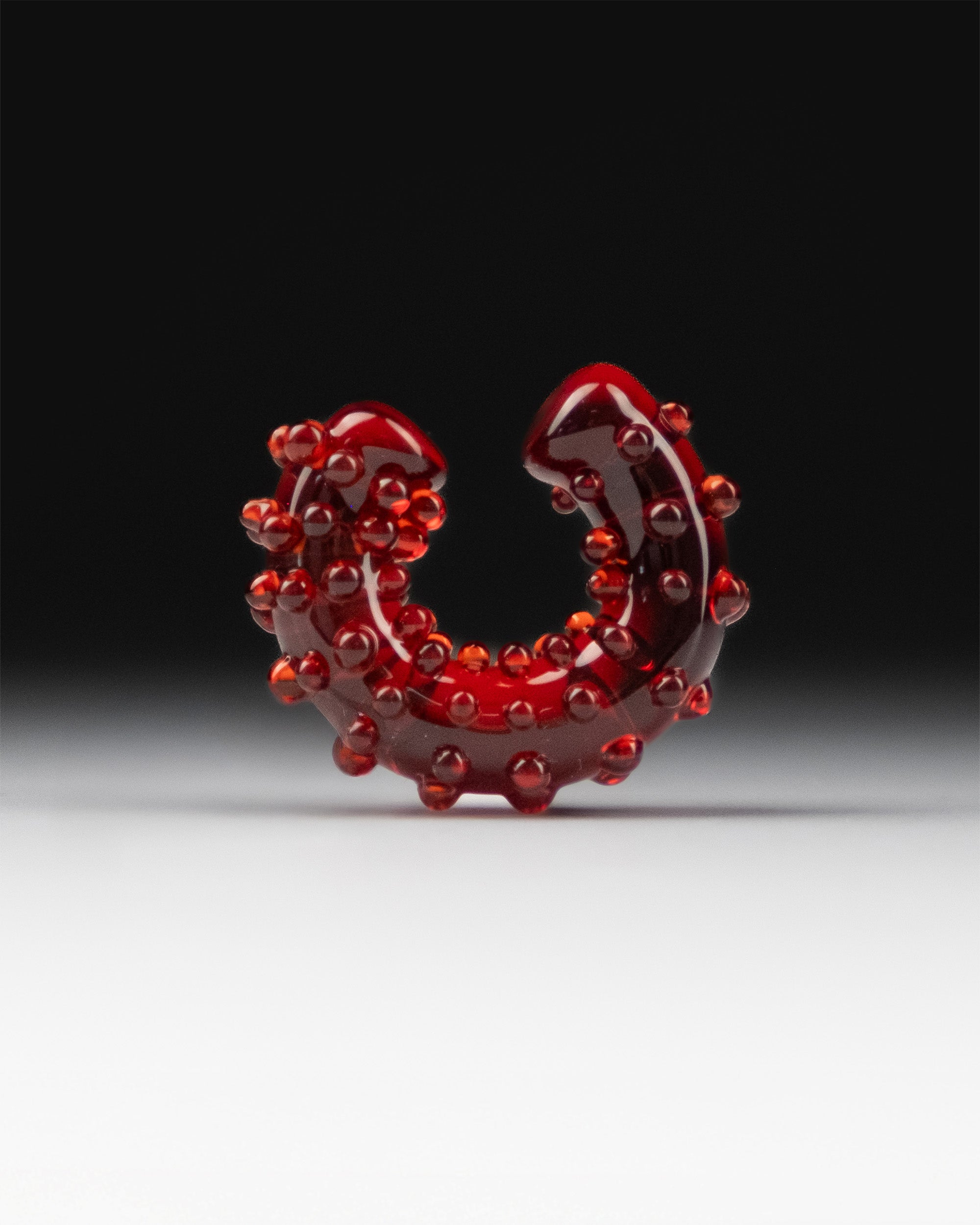 Full view of red glass ear cuff with sculptural dotted surface, designed for non-pierced wear.